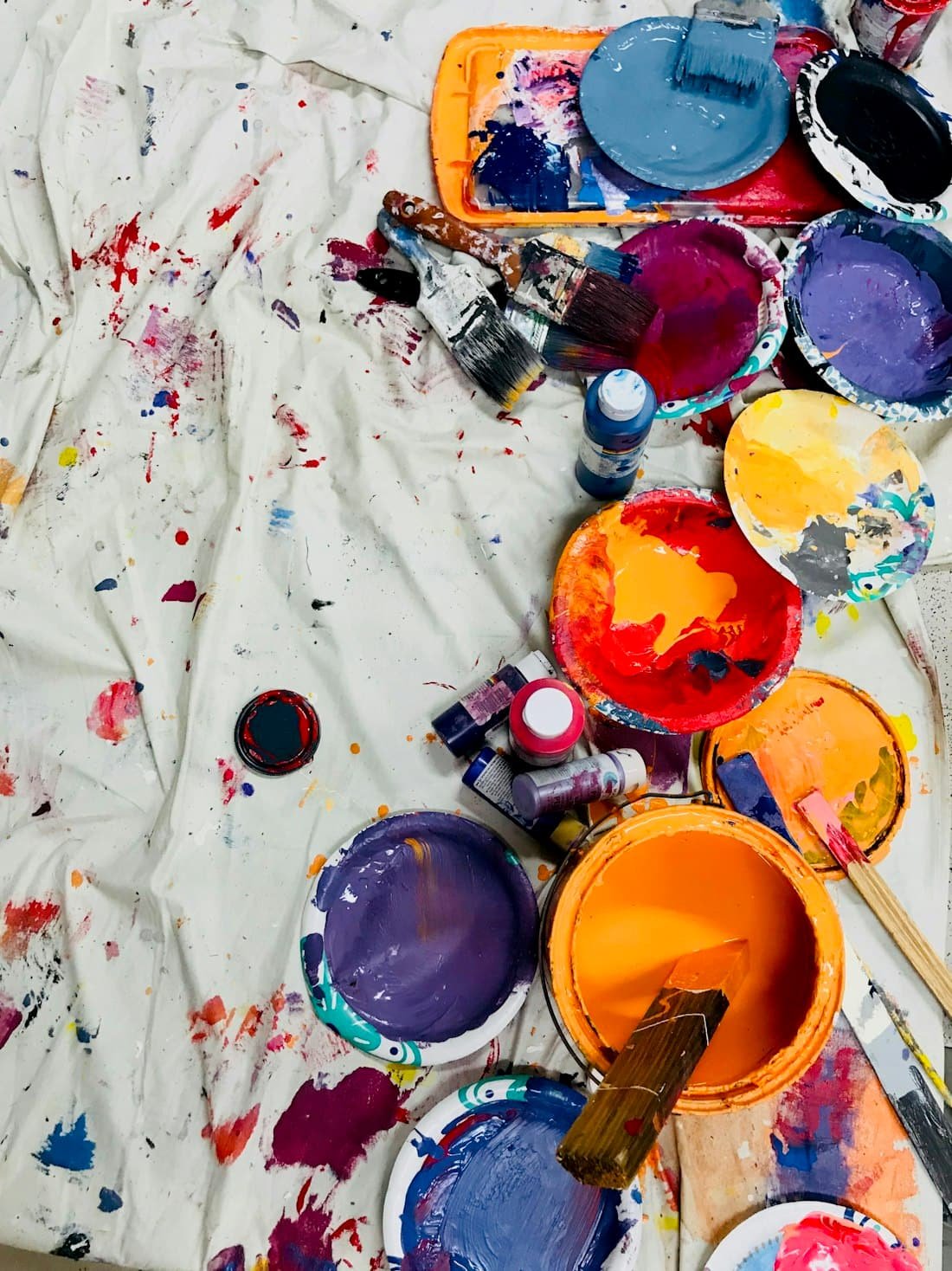 Assorted paint colours and brushes laid out on a drop sheet